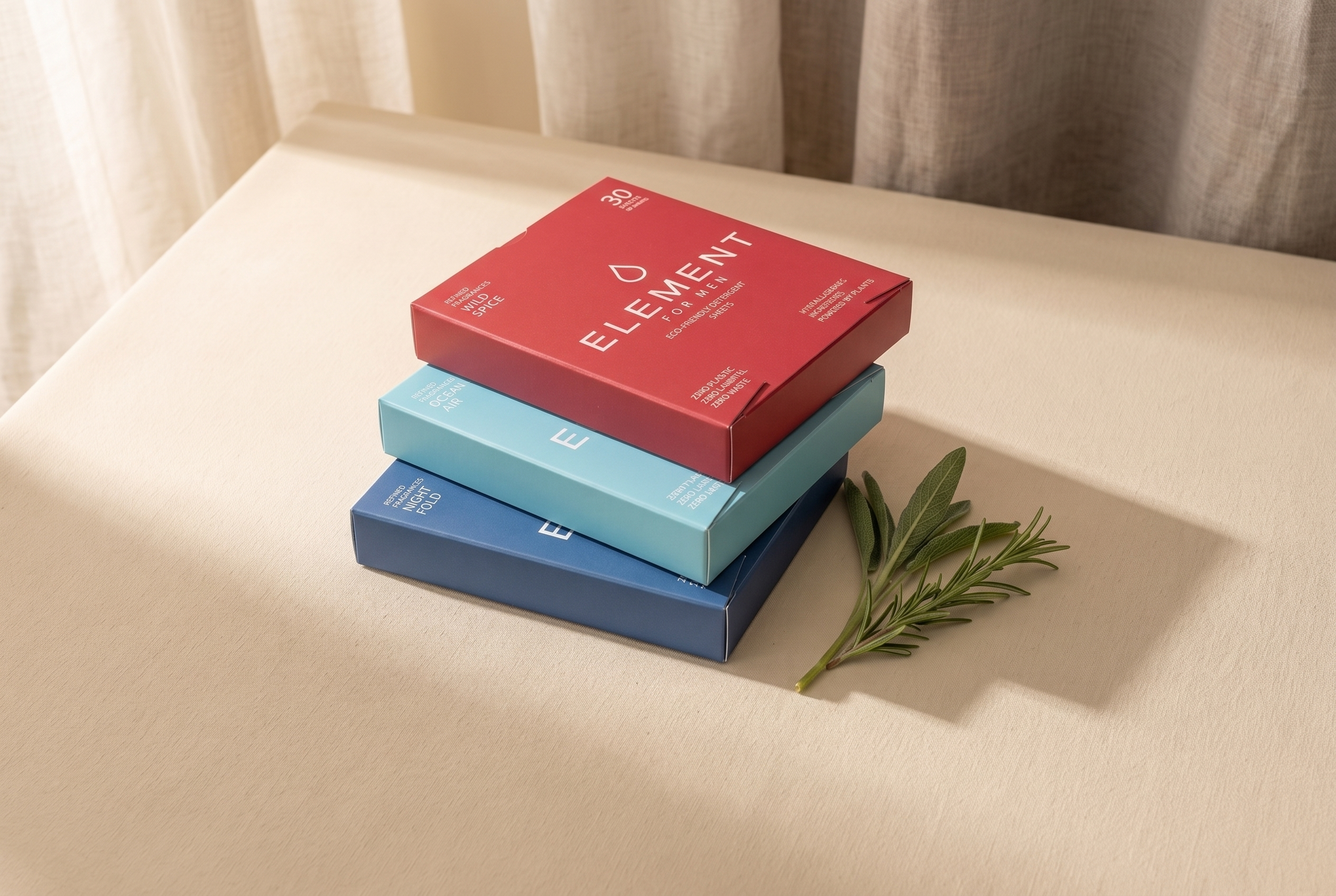 Three Element laundry detergent sheet boxes in their true colours — blue Night Fold, teal Ocean Air and red Wild Spice — arranged on a warm cream surface, comparing the UK's best smelling laundry detergent scents.