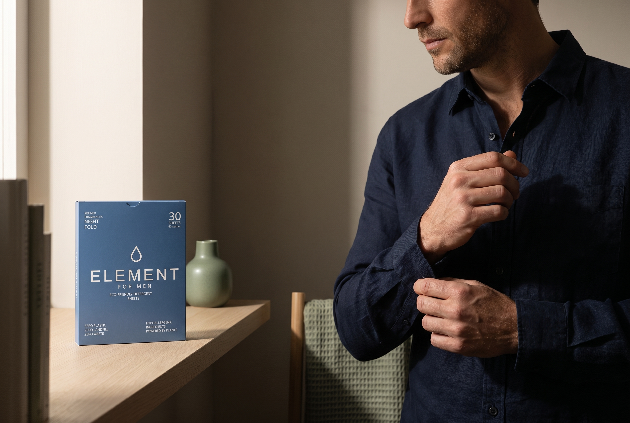 Man adjusting his navy shirt cuff in warm window light beside an Element for Men Night Fold detergent sheet box — why does my cologne fade so fast