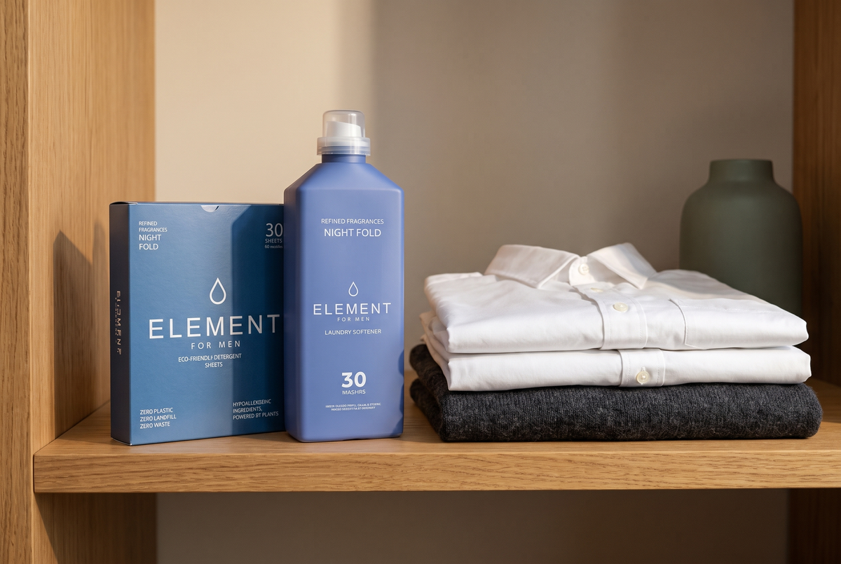 An Element for Men Night Fold fabric softener bottle and detergent sheet carton on an oiled oak wardrobe shelf beside folded white shirts and a charcoal wool jumper