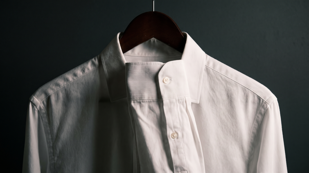 A white shirt collar and cuff on a wooden hanger against a charcoal background